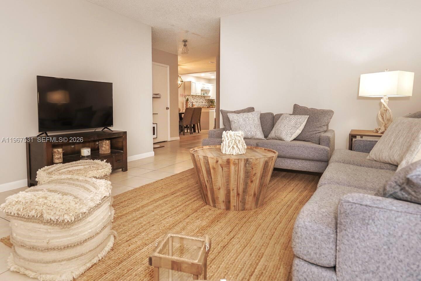 A living room features a gray sofa, a wooden coffee table, and a television stand — 20 SE 12th St, Dania Beach FL 33004, DANIA BEACH, FL