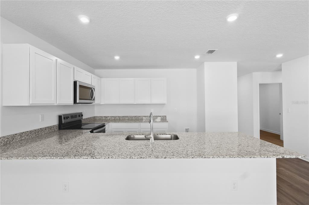A modern kitchen features white cabinets, granite countertops, and a central island with a sink — 16294 NW 143RD WAY, ALACHUA, FL