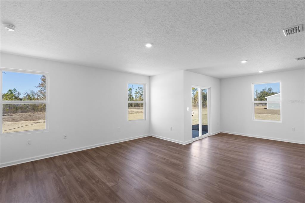 An empty room with white walls, wood-look flooring, recessed lighting, and sliding glass doors — 16294 NW 143RD WAY, ALACHUA, FL