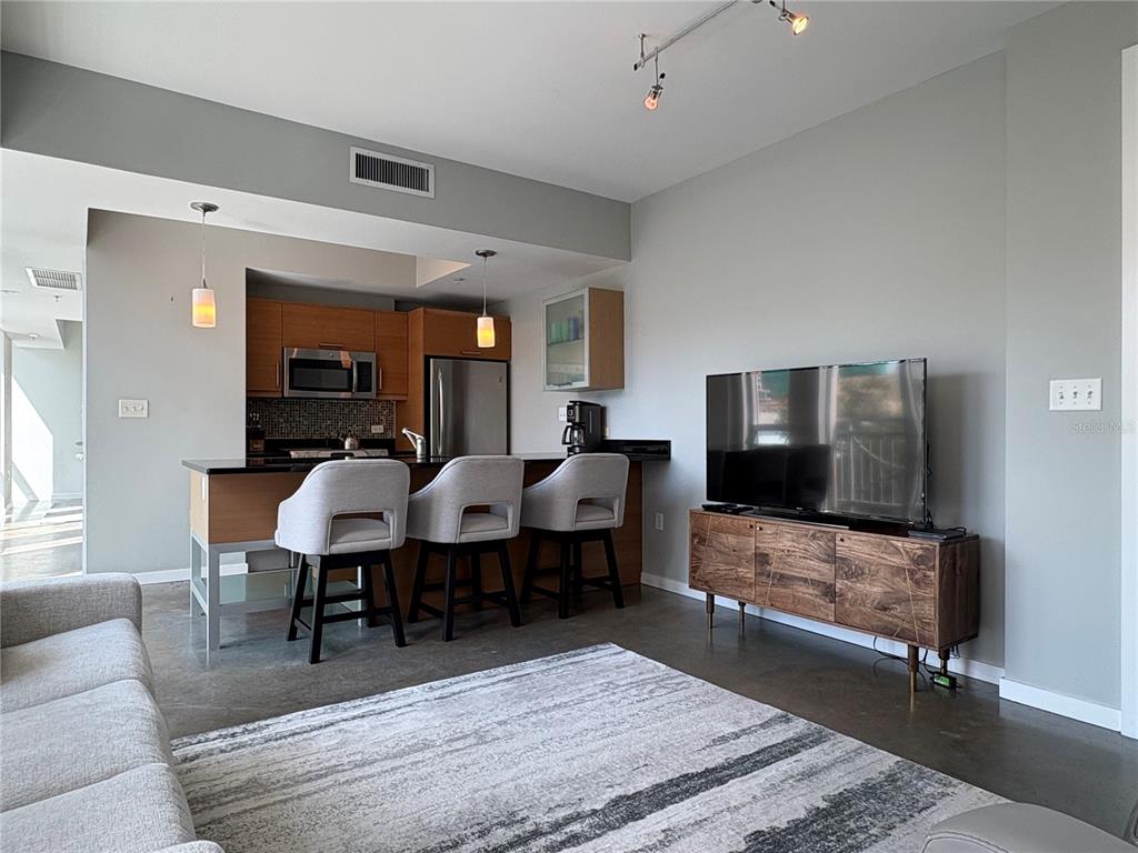 A modern living room and kitchen area with light wood cabinets, bar stools, and concrete floors — 1350 MAIN STREET UNIT 302, SARASOTA, FL