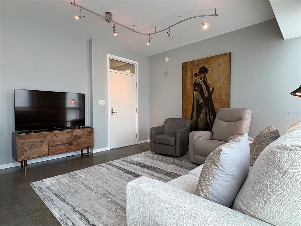 A living room features a television on a wooden console, two chairs, and track lighting — 1350 MAIN STREET UNIT 302, SARASOTA, FL