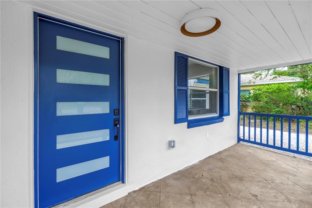 A covered porch features a bright blue front door, a window with blue shutters, and railings — 8171 37TH AVENUE N, ST PETERSBURG, FL