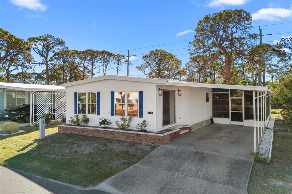 A single-story mobile home with white siding, blue shutters, a brick planter, and a carport — 177 S FIJI CIRCLE, ENGLEWOOD, FL