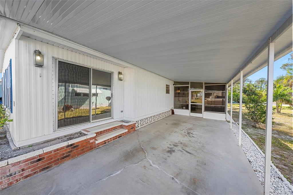 A covered concrete patio features a sliding glass door, brick steps, and white siding — 177 S FIJI CIRCLE, ENGLEWOOD, FL