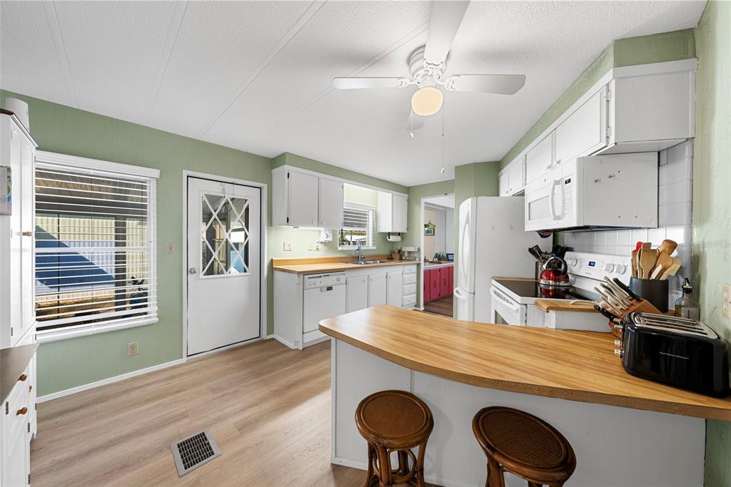 A kitchen with white cabinets, wood-look flooring, a breakfast bar, and a ceiling fan — 177 S FIJI CIRCLE, ENGLEWOOD, FL