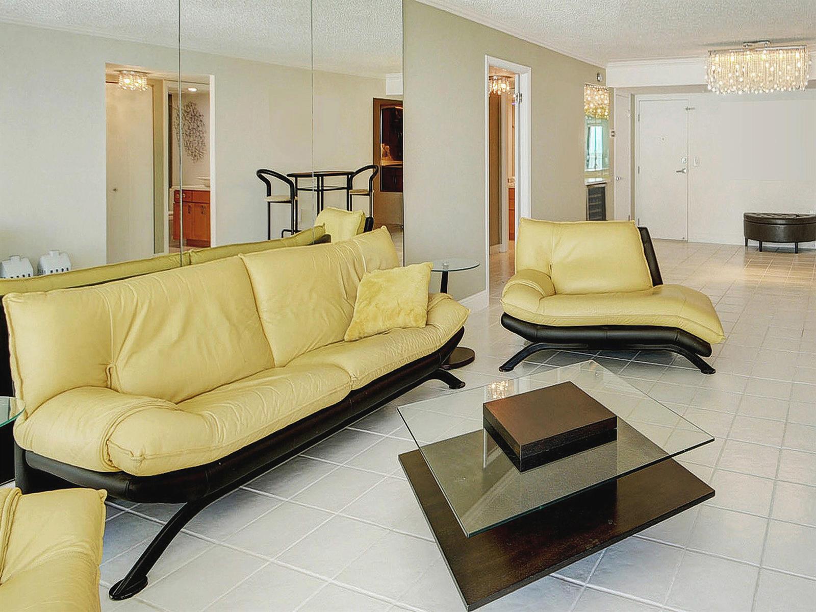 A living room features yellow leather furniture, a glass coffee table, and large wall mirrors — 3460 S Ocean Boulevard # 7110, Palm Beach FL 33480, PALM BEACH, FL