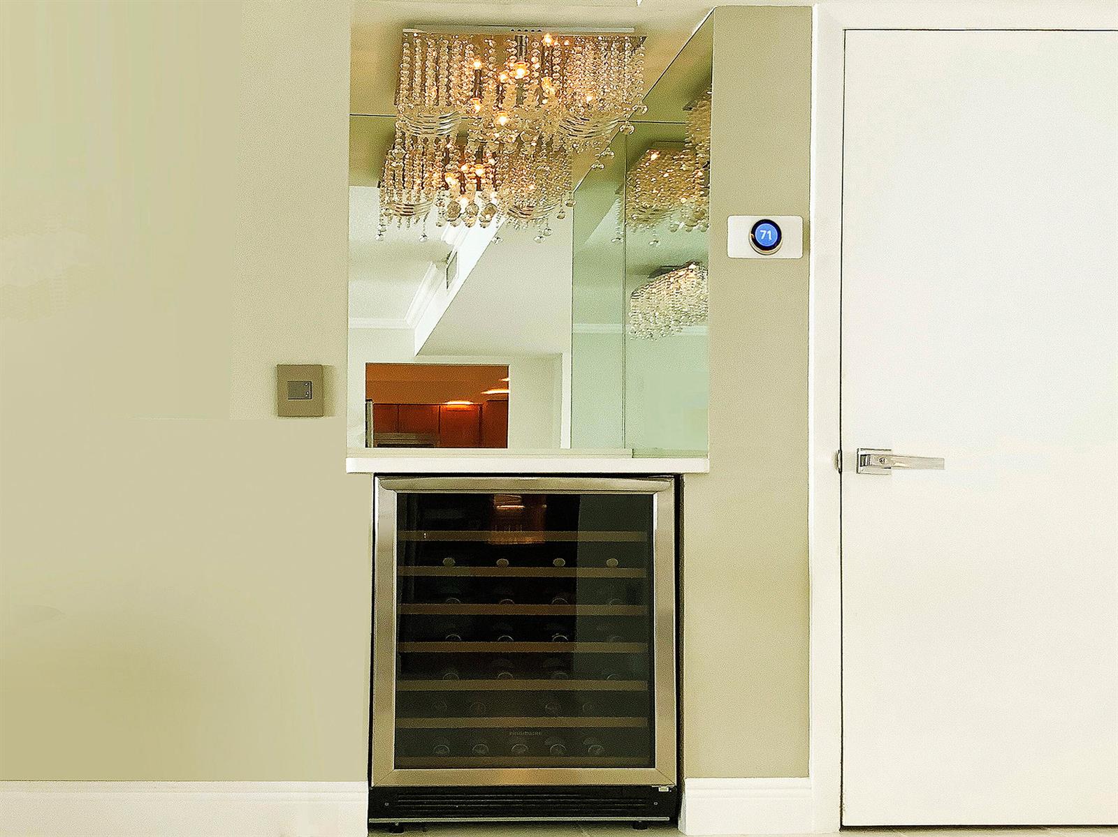 A wine refrigerator sits beneath a mirror and a crystal chandelier in a neutral room — 3460 S Ocean Boulevard # 7110, Palm Beach FL 33480, PALM BEACH, FL