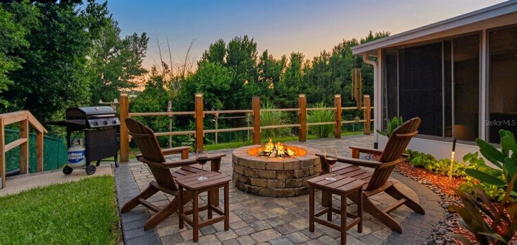 A stone fire pit sits on a paved patio with two wooden chairs and a grill — 1371 S PRAIRIE CIRCLE, DELTONA, FL