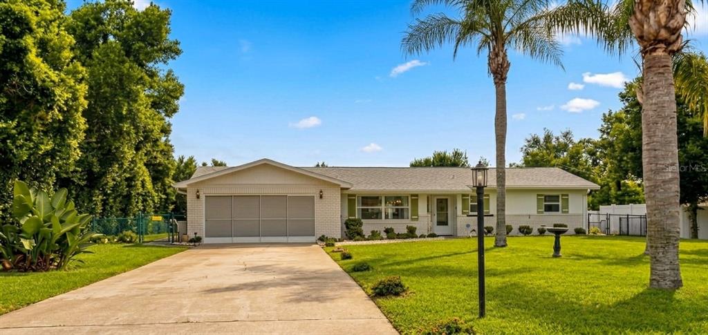 A single-story house with a white brick facade, a concrete driveway, and a palm tree — 1371 S PRAIRIE CIRCLE, DELTONA, FL