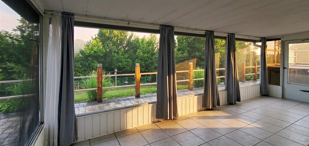A sunroom features tiled flooring, large screened windows, gray curtains, and a view of greenery — 1371 S PRAIRIE CIRCLE, DELTONA, FL