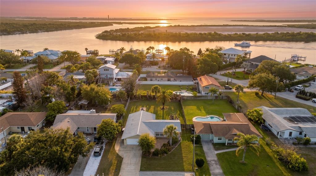 An aerial view shows a residential neighborhood with houses, swimming pools, and a sunset waterway — 40 CUNNINGHAM DRIVE, NEW SMYRNA BEACH, FL
