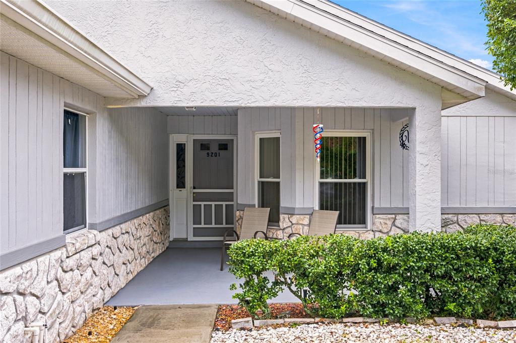 A covered front porch features a screen door, stone siding, and two outdoor chairs — 9201 SW 91ST CIRCLE, OCALA, FL
