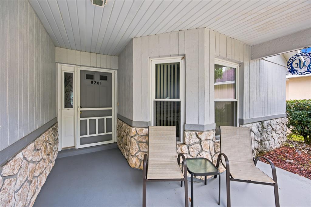 A covered front porch features a gray door, two chairs, a small table, and stone siding — 9201 SW 91ST CIRCLE, OCALA, FL