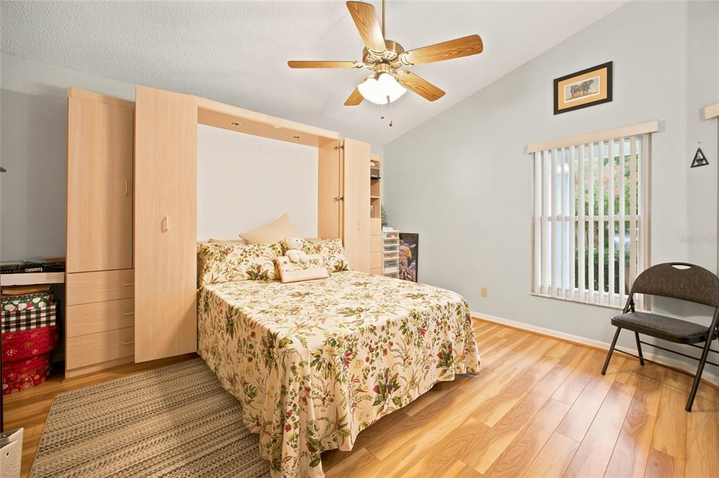 A bedroom features a light wood Murphy bed, floral bedding, a ceiling fan, and wood flooring — 9201 SW 91ST CIRCLE, OCALA, FL