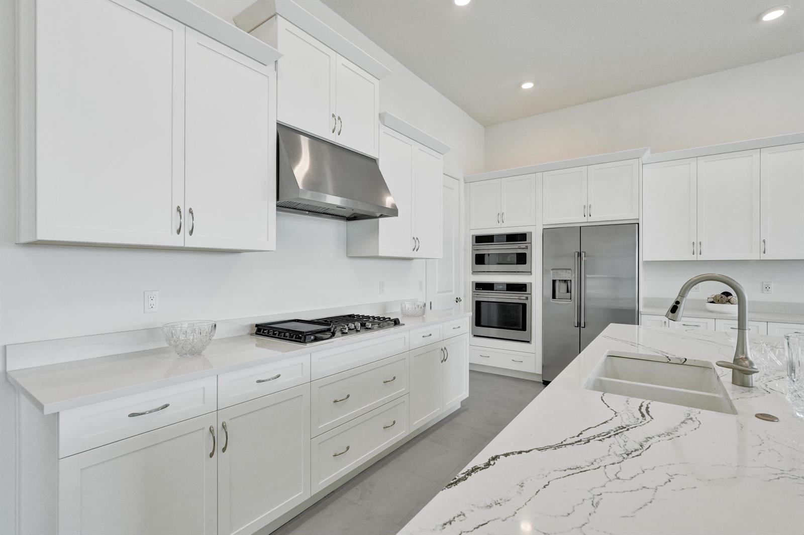 A modern kitchen features white cabinetry, stainless steel appliances, and a marble-patterned island countertop — 5183 Rivo Alto Circle, Westlake FL 33470, WESTLAKE, FL