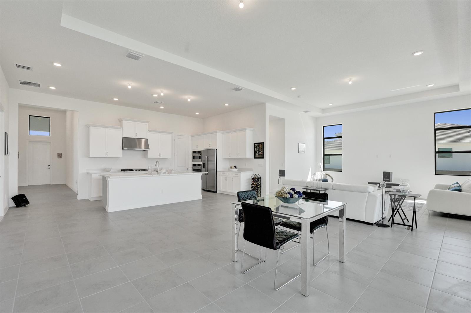 An open-concept kitchen and living area features white cabinetry, tile flooring, and modern furniture — 5183 Rivo Alto Circle, Westlake FL 33470, WESTLAKE, FL