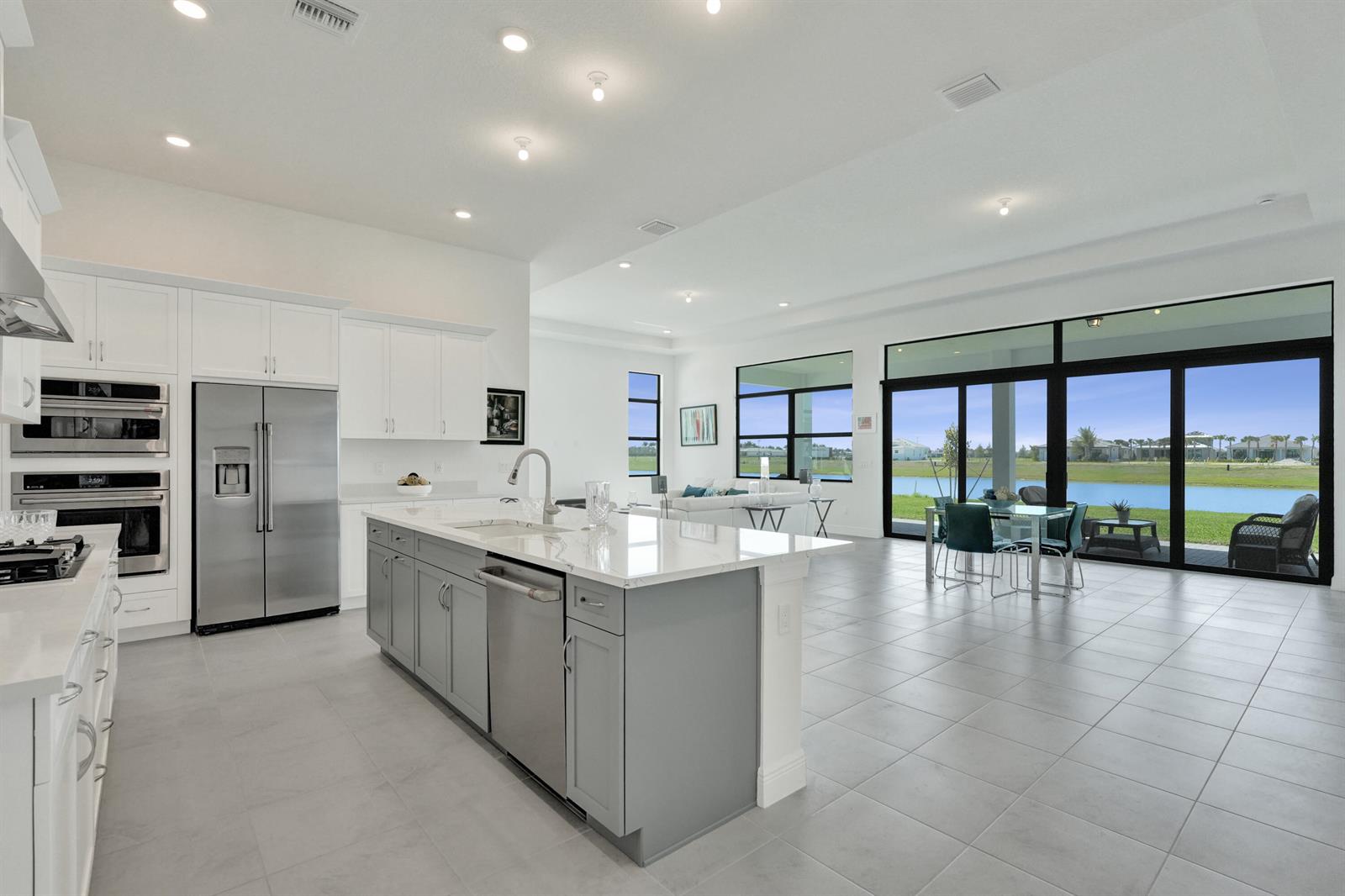 A modern kitchen with a gray island and white cabinets overlooks a living area and lake — 5183 Rivo Alto Circle, Westlake FL 33470, WESTLAKE, FL
