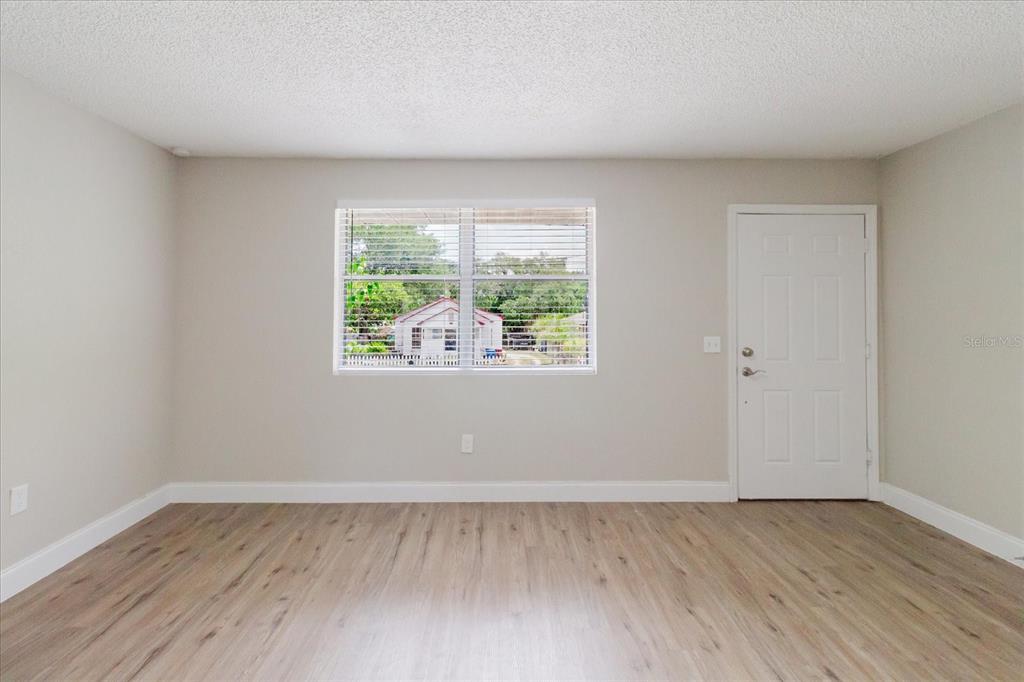 An empty room with light wood-look flooring, beige walls, a window, and a white door — 1134-1136 GILMORE AVENUE, LAKELAND, FL