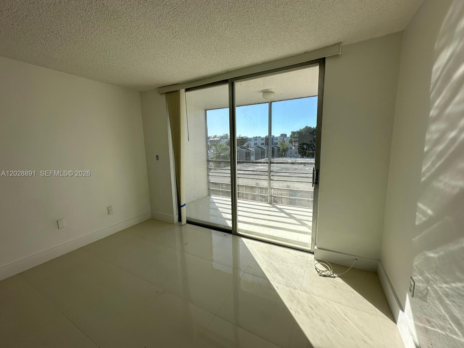 An empty room features white walls, light-colored tile flooring, and a sliding glass door to a balcony — 14170 SW 84th St # F, Miami FL 33183, MIAMI, FL
