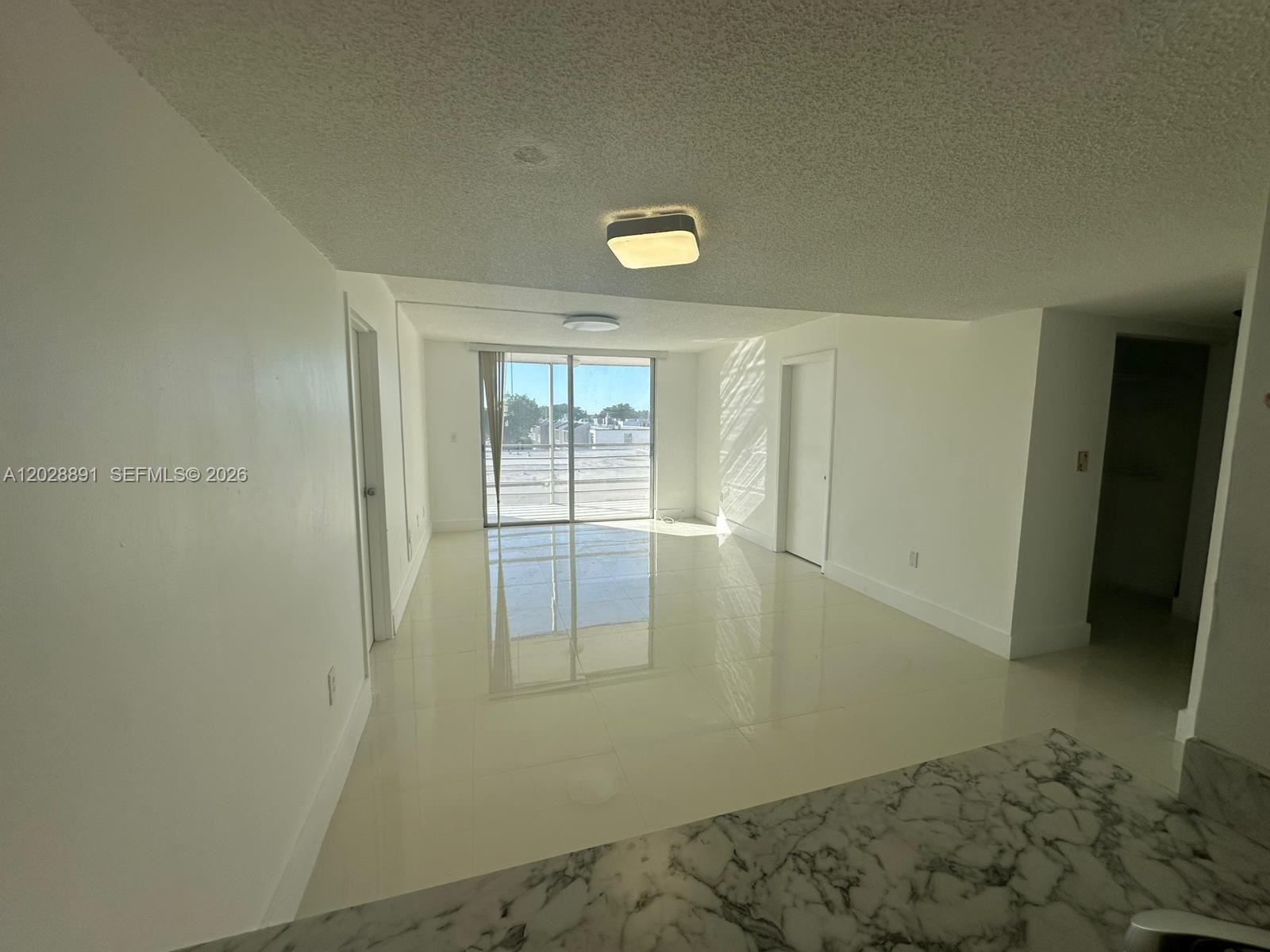 An empty room features white walls, glossy tile flooring, and a sliding glass balcony door — 14170 SW 84th St # F, Miami FL 33183, MIAMI, FL