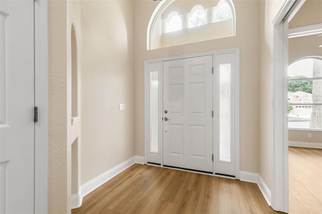 A bright entryway features light wood-look flooring, a white front door, and a high arched window — 21 VILLAGE VIEW DRIVE, PALM COAST, FL