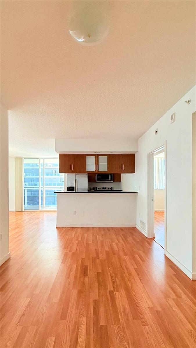 An interior view of a living area with wood flooring, a kitchen, and a balcony — 601 NE 23rd Street # 902, Miami FL 33137, MIAMI, FL