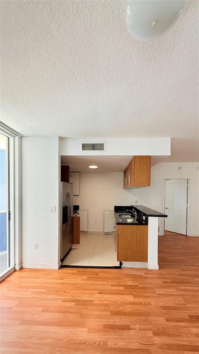 A kitchen with wood cabinets and black countertops opens into a living area with wood flooring — 601 NE 23rd Street # 902, Miami FL 33137, MIAMI, FL