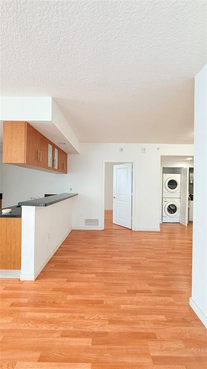 An interior view showing a kitchen with a breakfast bar, wood flooring, and stacked laundry — 601 NE 23rd Street # 902, Miami FL 33137, MIAMI, FL