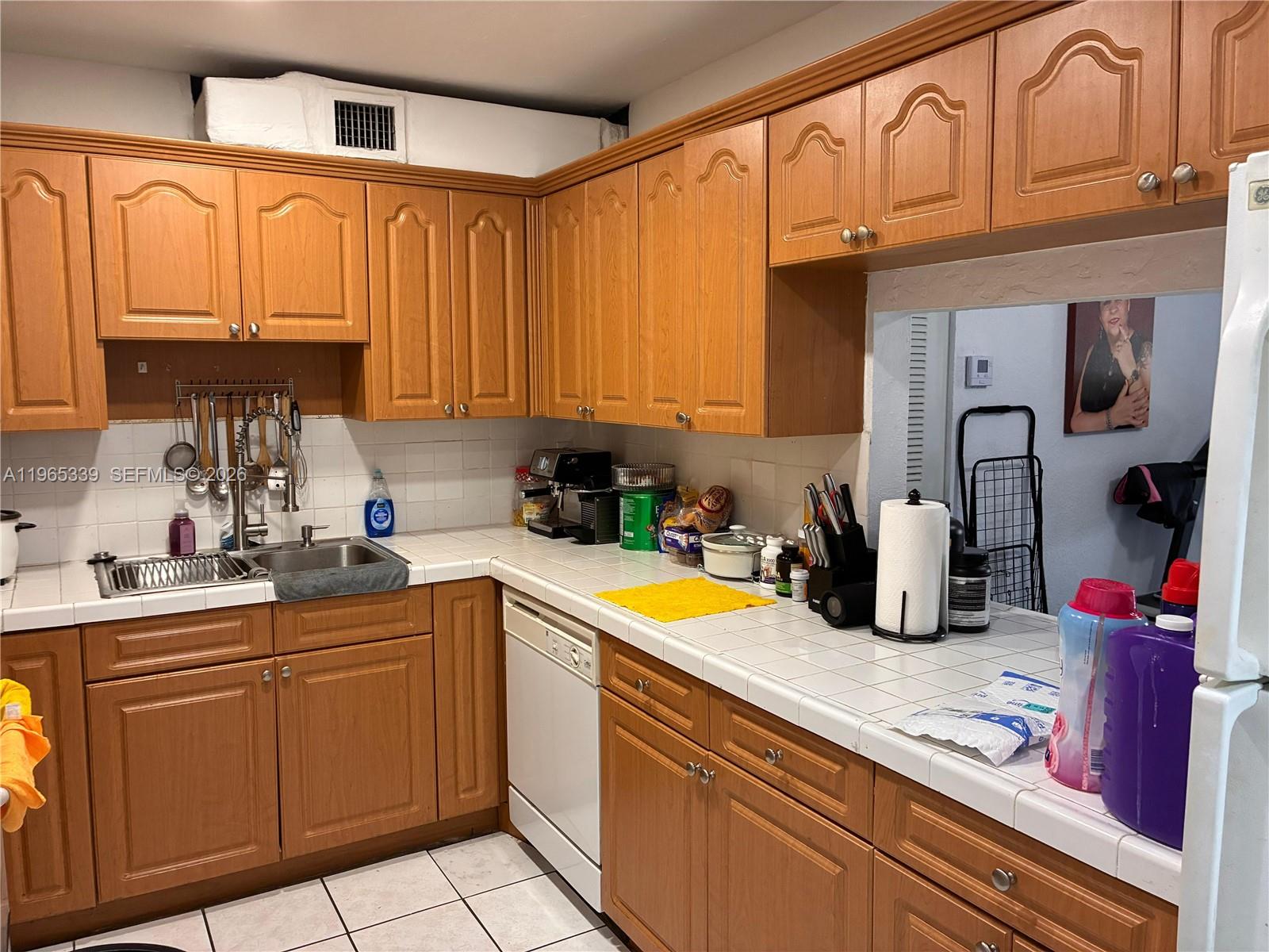 A kitchen features wood cabinets, white tile countertops, and a white dishwasher — 1900 W 68th St # G103, Hialeah FL 33014, HIALEAH, FL