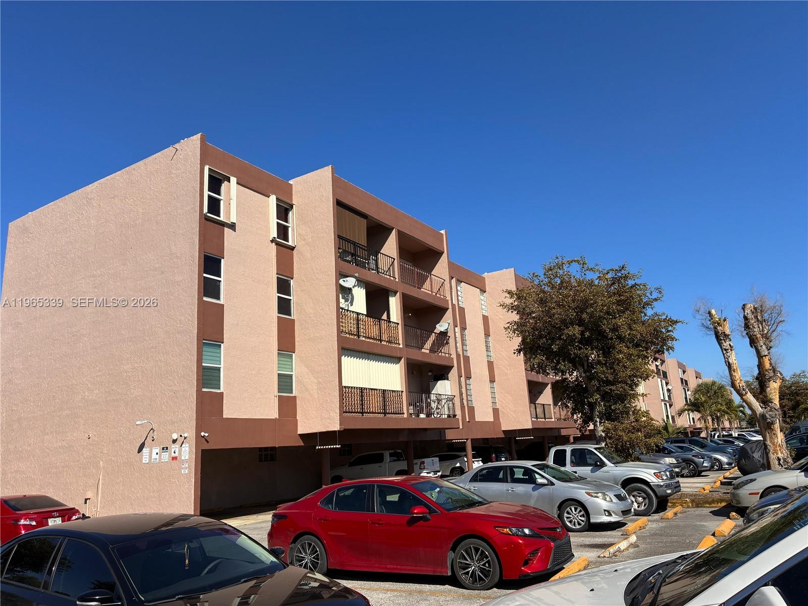 A multi-story apartment building with covered parking and several parked cars in front — 1900 W 68th St # G103, Hialeah FL 33014, HIALEAH, FL