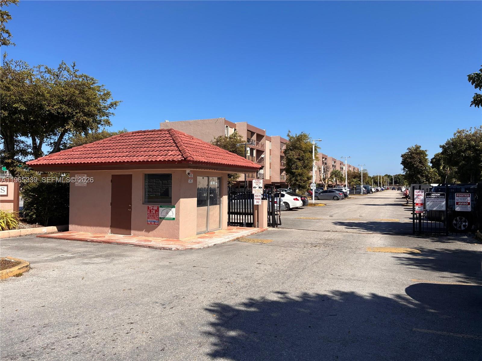 An exterior view of a small guardhouse with a red tile roof and parking area — 1900 W 68th St # G103, Hialeah FL 33014, HIALEAH, FL