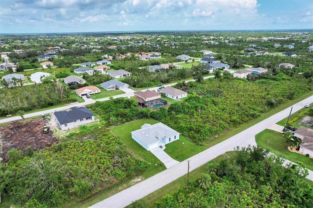An aerial view shows a suburban neighborhood with scattered single-family homes and undeveloped wooded lots — 9245 ZORN STREET, PORT CHARLOTTE, FL