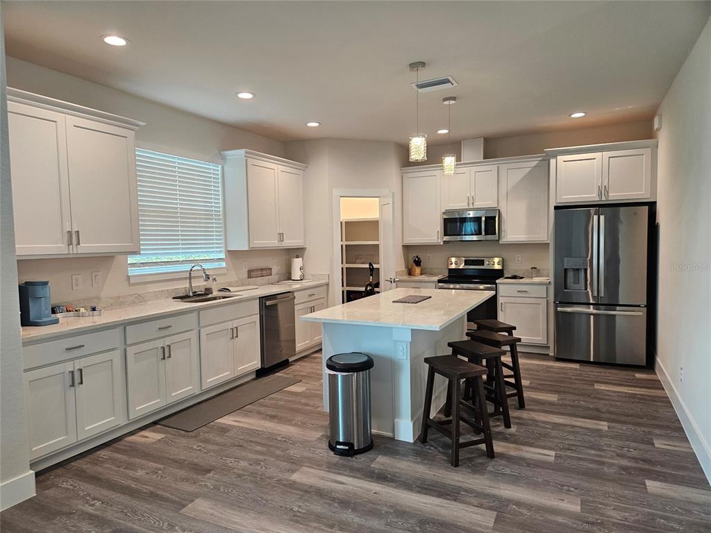 A kitchen features white cabinets, stainless steel appliances, a center island, and wood-look flooring — 9245 ZORN STREET, PORT CHARLOTTE, FL
