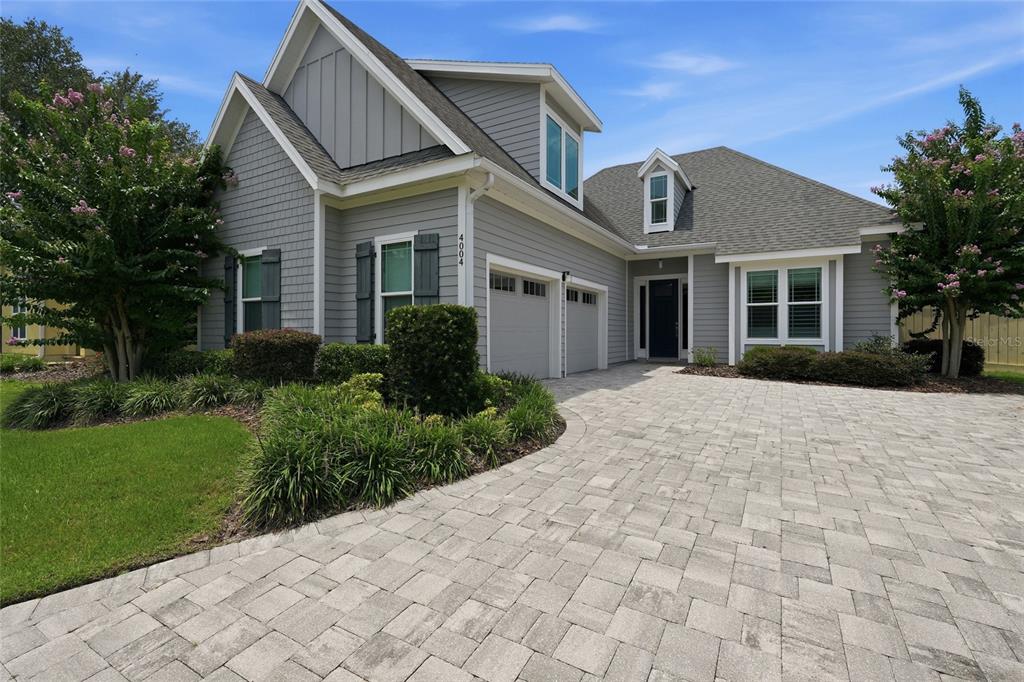 A gray two-story house features a paver driveway, a two-car garage, and landscaped front gardens — 4004 NW 63RD STREET, GAINESVILLE, FL