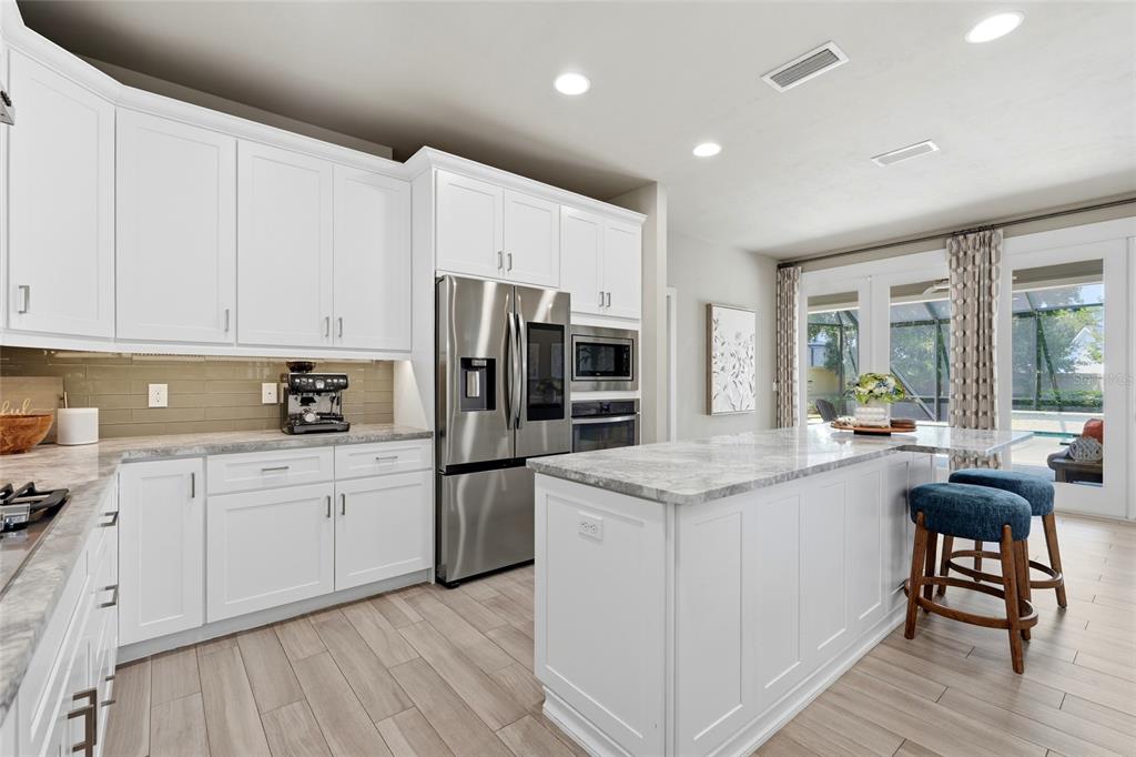 A modern kitchen features white cabinetry, stainless steel appliances, a marble island, and wood-look flooring — 4004 NW 63RD STREET, GAINESVILLE, FL