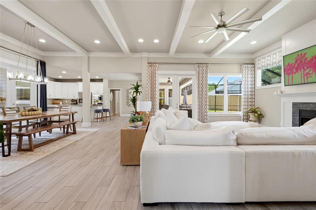 An open-concept living and dining area features light wood flooring, white coffered ceilings, and a sectional — 4004 NW 63RD STREET, GAINESVILLE, FL