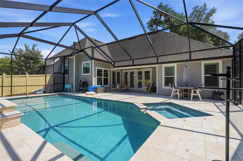 A screened-in patio features a swimming pool, a hot tub, and light-colored stone pavers — 4004 NW 63RD STREET, GAINESVILLE, FL