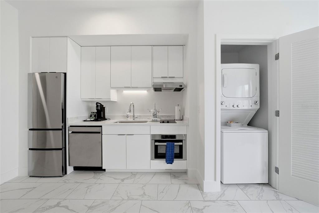 A small kitchen with white cabinets, stainless steel appliances, and a laundry closet with stacked units — 411 E SHORE DRIVE UNIT 403, CLEARWATER BEACH, FL