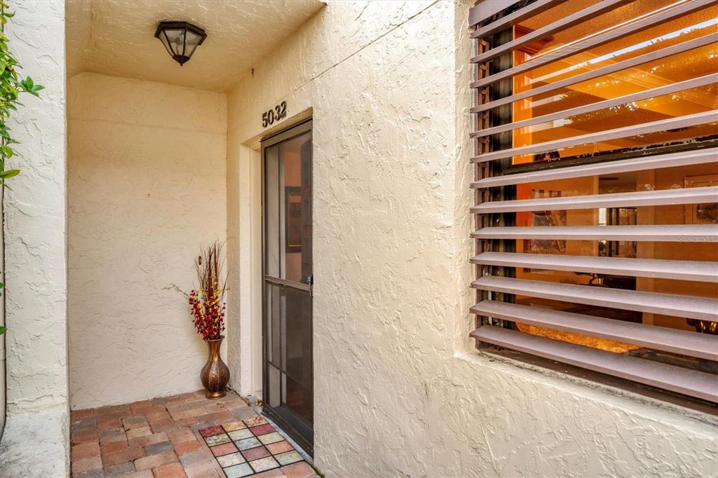 A beige stucco entryway features a screen door, a decorative vase, and horizontal window shutters — 5032 MARSHFIELD ROAD UNIT 19, SARASOTA, FL