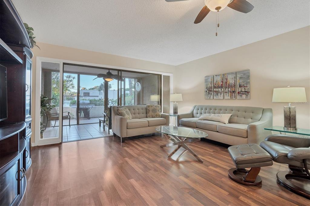 A living room with wood-look flooring, a sofa, a loveseat, and sliding doors to a patio — 5032 MARSHFIELD ROAD UNIT 19, SARASOTA, FL