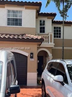 A two-story stucco house exterior features a garage, a balcony, and two parked cars — HOLLYWOOD, FL