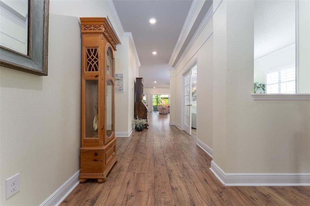 A hallway with wood-look flooring leads toward a bright living area featuring a grandfather clock — 14008 SWALLOW HILL DRIVE, LITHIA, FL