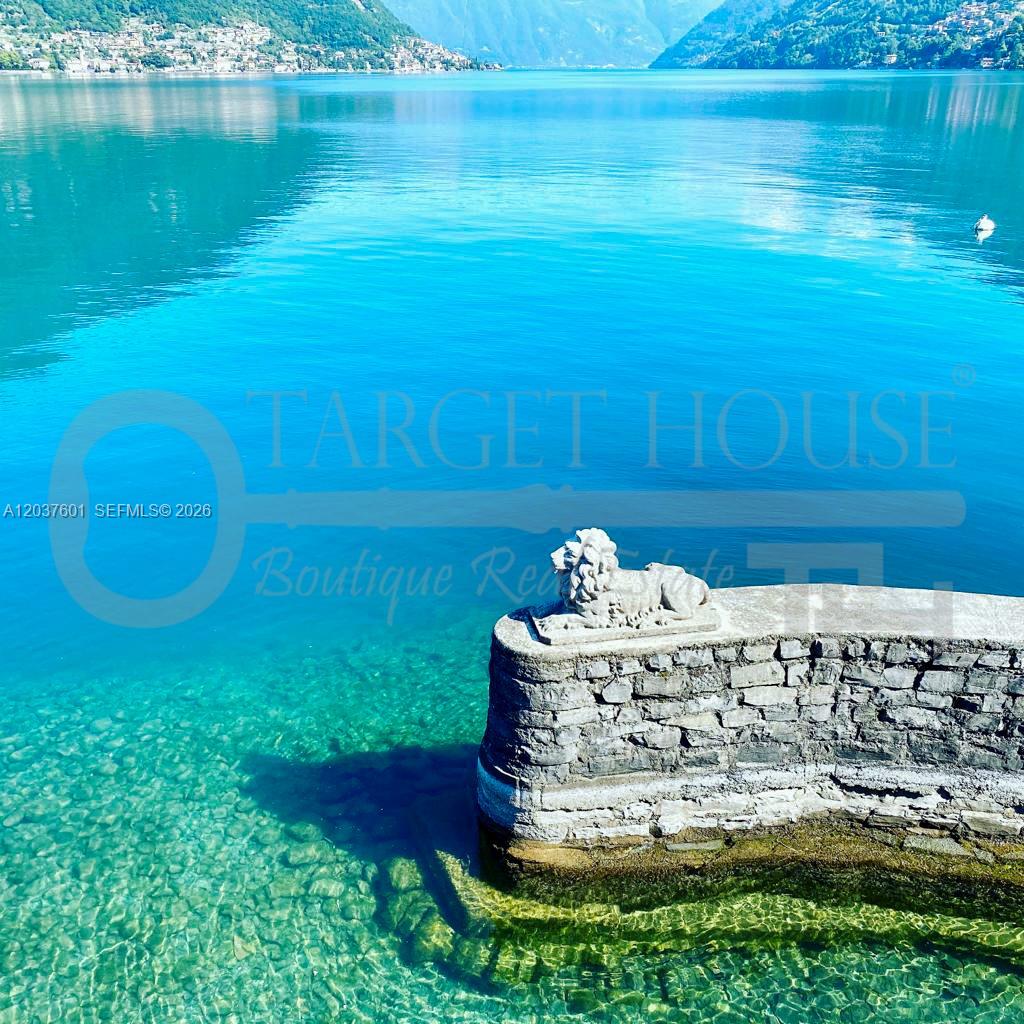 A stone wall with a lion statue overlooks a clear blue lake with mountains — lago di Como lake front, VA 22100, VA