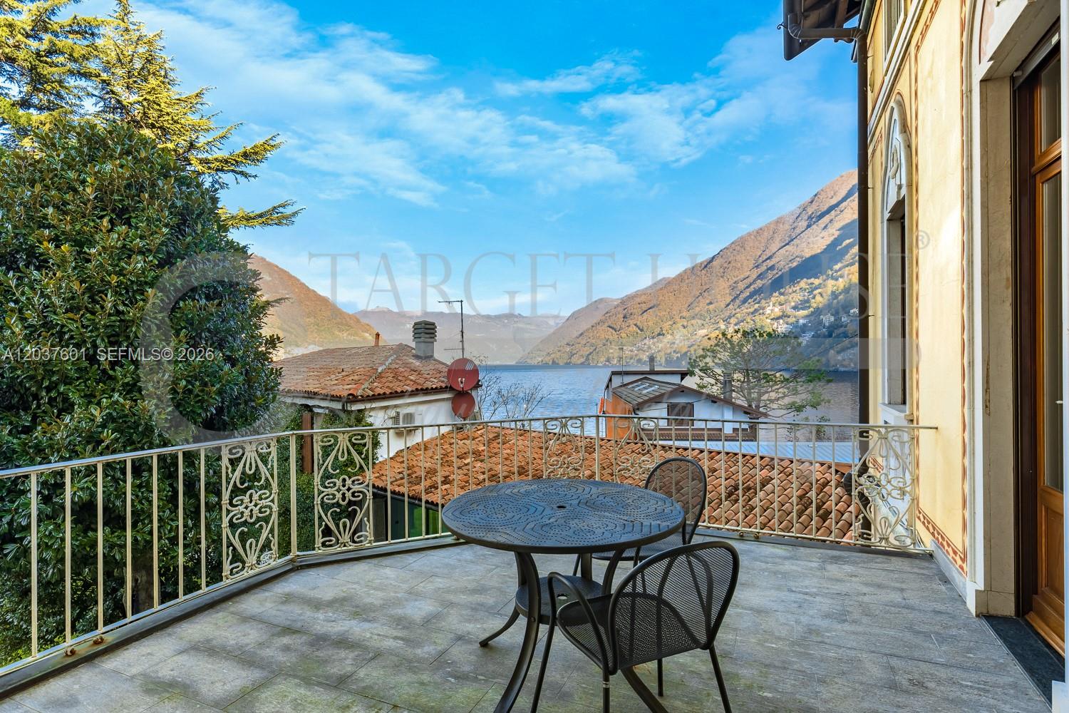A balcony with a metal table and chairs overlooks a lake and mountain landscape — lago di Como lake front, VA 22100, VA