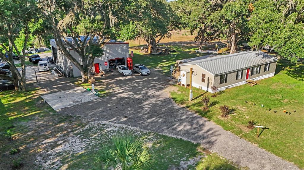 An aerial view shows a metal workshop, a manufactured home, and vehicles on a gravel lot — 12709 CHIHUAHUA COURT, THONOTOSASSA, FL