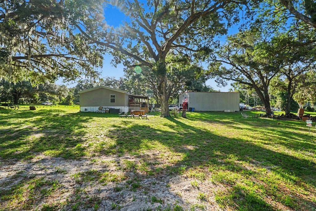 A mobile home and a detached metal workshop sit on a large, tree-shaded grassy lot — 12709 CHIHUAHUA COURT, THONOTOSASSA, FL