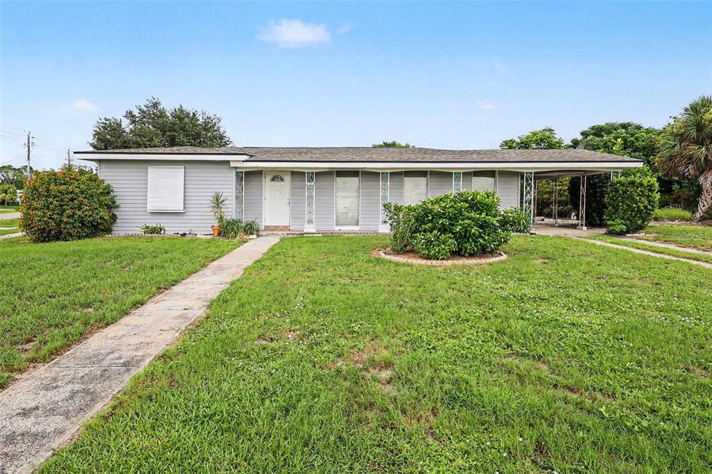 A single-story house with gray siding, a front porch, and a carport under a blue sky — 21422 MALLORY AVENUE, PORT CHARLOTTE, FL