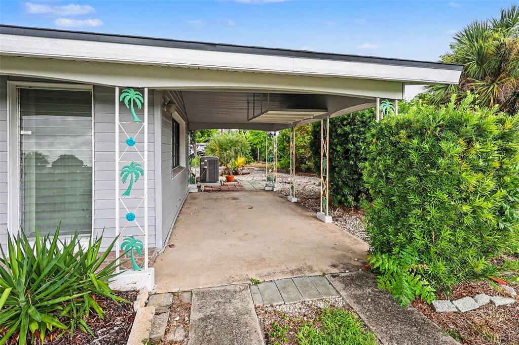 A concrete carport features decorative metal palm tree supports attached to a gray house — 21422 MALLORY AVENUE, PORT CHARLOTTE, FL