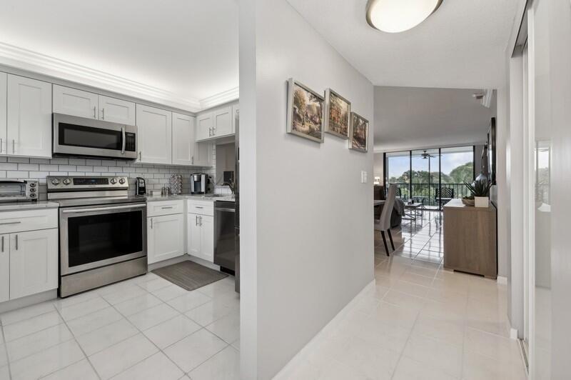 A white kitchen with stainless steel appliances opens into a bright living area with balcony — 6530 Boca Del Mar Drive # 337, Boca Raton FL 33433, BOCA RATON, FL