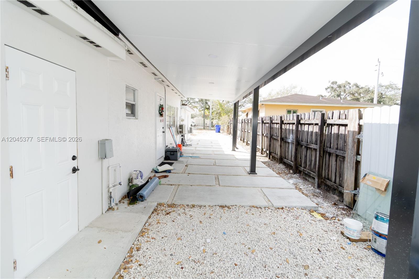 A covered concrete patio runs alongside a white house with a wooden fence nearby — 5803 Buchanan St, Hollywood FL 33021, HOLLYWOOD, FL